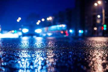 Rainy night in the big city, the approaching car headlights shine through the mist. Close up view from the asphalt level