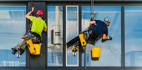 Two men cleaning windows on an office building - obrazy, fototapety, plakaty