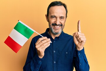 Middle age hispanic man holding italy flag smiling with an idea or question pointing finger with happy face, number one