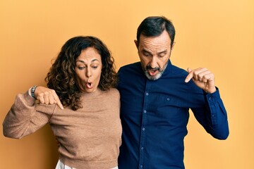 Obraz premium Middle age hispanic couple wearing casual clothes pointing down with fingers showing advertisement, surprised face and open mouth