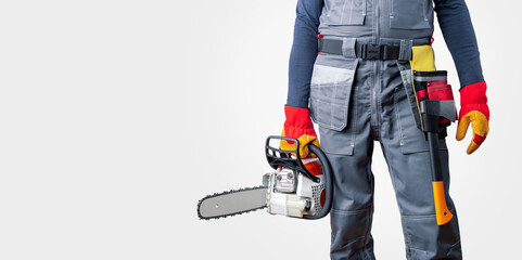  Man in uniform holding a chainsaw on a grey background with copy space. Banner.  Concept building, contractor, repair, lumberjack.