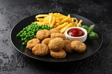 Fried crispy chicken nuggets with ketchup, french fries and green peas in black plate