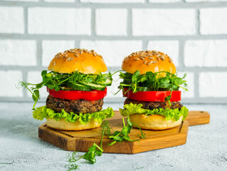 Vegetarian burgers with bean burger and fresh vegetables on a homemade saucer on a wooden board on a light concrete background. Burgers recipes.