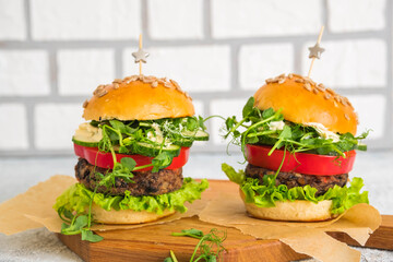 Vegetarian burgers with bean burger and fresh vegetables on a homemade saucer on a wooden board on a light concrete background. Burgers recipes.
