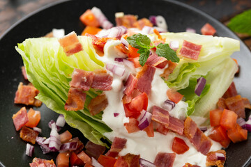 Iceberg wedge salad with bacon, cherry tomatoes, red onion and dressing. healthy food