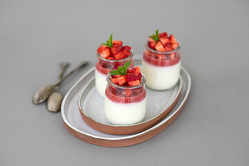 Italian dessert panna cotta with fruit jelly and fresh pieces of strawberries on gray background. Copy space