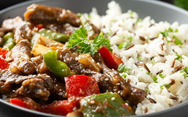 Stir fry Chinese pepper beef steak with onion, red and green bell pepper, rice in bowl