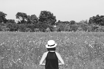 Woman wearing black dress and white vintage hat standing back among cosmos flower garden park with tree and sky background in black and white tone. People with nature and plant in monochrome picture. 