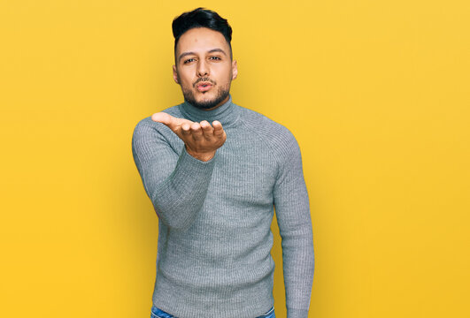 Young arab man wearing casual clothes looking at the camera blowing a kiss with hand on air being lovely and sexy. love expression.