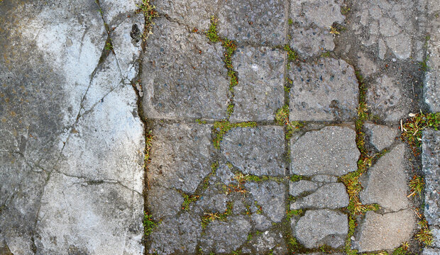 broken tiles and cement from an olf floor in the street with grass between the cracks - closeup rough texture
