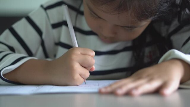closeup hand of asian child student or kid girl writing and doing homework on book or read to learn from home and training write on paper and desk by stay safe and back to school study online on 4K