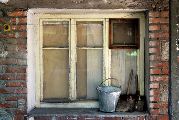 old window with white frames and a weathered bucket on the windowsill - abandoned facade with retro brick background