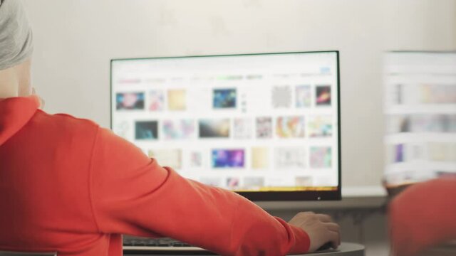 A programmer in a gray hat works in a home office in the evening sitting at a monitor screen