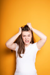 Fototapeta na wymiar Angry young girl with braces pulls out the hair on her head from pain in the teeth and in the head while standing on a yellow background