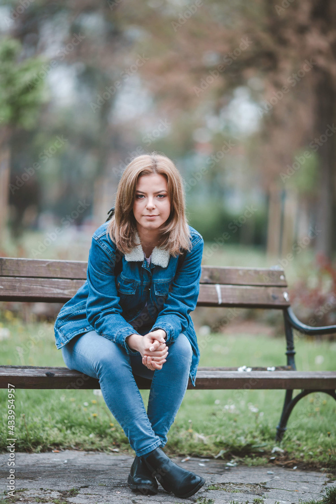 Sticker shallow focus shot of a blonde caucasian woman wearing a jean jacket sitting in the park