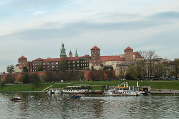 Fototapeta na wymiar A panoramic view on the iconic Wawel Castle in Cracow, Poland and the Vistula river flowing under the castle. A few birds flying above the river. A few boats docked on the rivers bend. City tour.