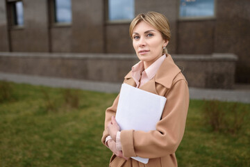 A beautiful business woman in a coat stands with documents .