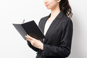 白バックの前に立って、ノートにメモを書くビジネスウーマン