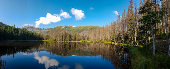 A panoramic view on Smreczynski Staw in Tatra Mountains in Poland. Glacial tarn at the mouth of Pysznianska Valley. The high Tatra chains are reflecting in the calm surface of the lake. White clouds © Chris