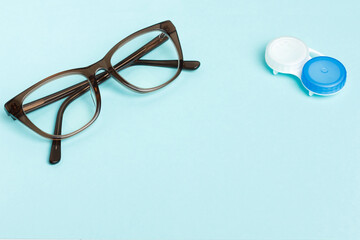 Glasses and lenses for vision correction on a colored background, top view. Ophthalmologist accessories. Improvement and prevention on a light surface. Plastic container