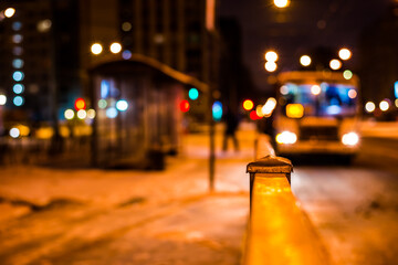 Winter night in the big city, the bus arrives to a stop for passengers. Close up view from the handrail on the sidewalk level