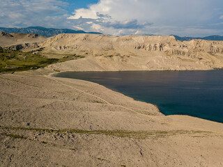 Aerial view of Rucica beach on Pag island, Metajna, Croatia. Seabed and beach seen from above, bathers, relaxation and summer holidays. Promontories and cliffs of Croatian coasts