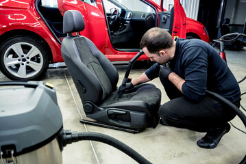 Fototapeta na wymiar Car service worker cleaning car seat with vacuum cleaner.