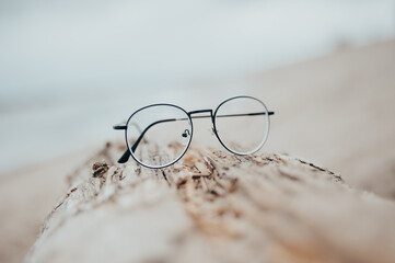 Womens beautiful glasses lie on a narrow beam on the beach on a blurred background