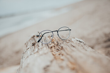 Fototapeta na wymiar Womens beautiful glasses lie on a narrow beam on the beach on a blurred background