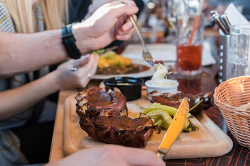 Close up of young man eating rib steak on wooden tray at restaurant.