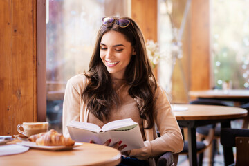 Attractive young woman sitting in the cafe and reading a book
