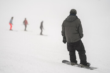 Fototapeta na wymiar Unidentified tourist does snowboard skiing in Flachau, the ski resort in Austria. Man in black and grey sportswear. People on bokeh background. Foggy weather.