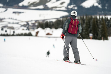 Fototapeta na wymiar Unidentified tourist skiing in Flachau, the ski resort in Austria. Man in grey sportswear and with red bag. People on bokeh background. View from behind.