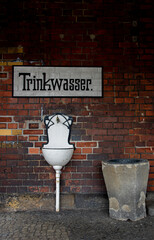 Public white drink water fountain on a red brick wall. The German script painted above reads "Drink water"