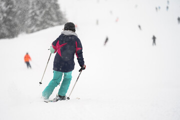 Unidentified tourist skiing in Flachau, the ski resort in Austria. Man in grey sportswear and with red bag. People on bokeh background. View from behind.