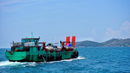 The cargo ship is traveling in the sea to the island.
