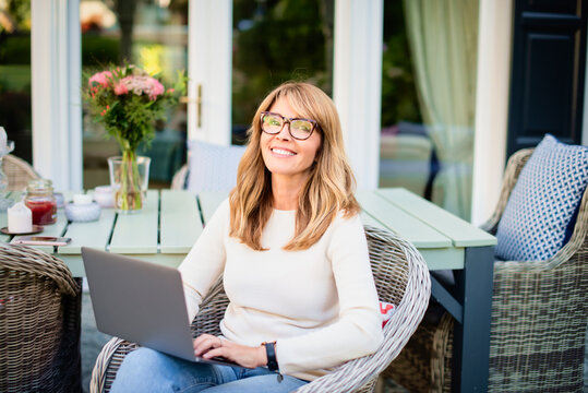 Attractive cheerful woman using laptop while sitting in the balcony at home