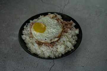 Obraz na płótnie Canvas black plate with cooked rice, fried egg and tuna on the table