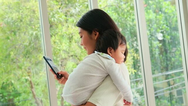 An Asian family mother holds her baby while talking on the phone for business. Work in parallel with raising babies for the family.