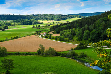 Fototapeta na wymiar Beautiful fresh green meadows, cultivated fields and a small river in a valley surrounded by forested hills in Germany.