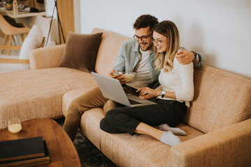 Obraz premium Young couple using laptop together while sitting on sofa at home