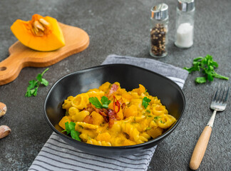 Pasta with pumpkin, fried bacon and hot peppers in a black plate on a dark concrete background. Pasta recipes.