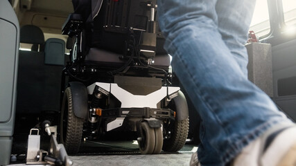 Assistant helping disabled person on wheelchair with transport using accessible vehicle ramp