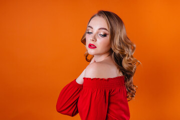 Fototapeta premium A young beautiful girl shows emotions and smiles in the Studio on an orange background. Girls for advertising