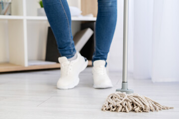 Cleaning home. Janitor woman. Chores hygiene. Enjoying result. Housework service. Unrecognizable woman legs in jeans sneakers shoes staying with mop light room interior.
