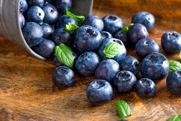  Blueberries are scattered from a metal bucket on a wooden table close-up, photo with soft focus