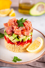 Salmon tartare with tomatoes, avocado and quinoa on a plate and light gray background close up, vertical photo