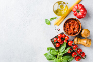 Italian cuisine food ingredients, marinara tomato sauce, cherry tomatoes, uncooked pasta, basil leaf and olive oil. Top view copy space