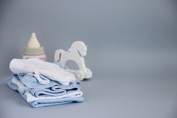 Clothes for small children with a toy horse and a bottle milk on a gray background.
