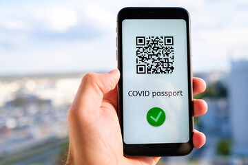 Covid pass with QR code on the screen in smartphone in mans hand on the background of cityscape